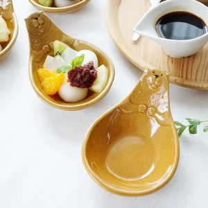 三個Yoshizawa 益子燒碟子在餐桌上，前面的盤子空著，後面的兩個盤子盛有食物 - Three Yoshizawa Mashiko-style plates on a dining table, with the front plate empty and the two back plates containing food.