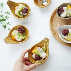 從上方視角顯示餐桌，前面的盤子被兩個手指握住，所有盤子上都有甜點 - Top view of a dining table, with the front plate held by two fingers and all plates featuring desserts.