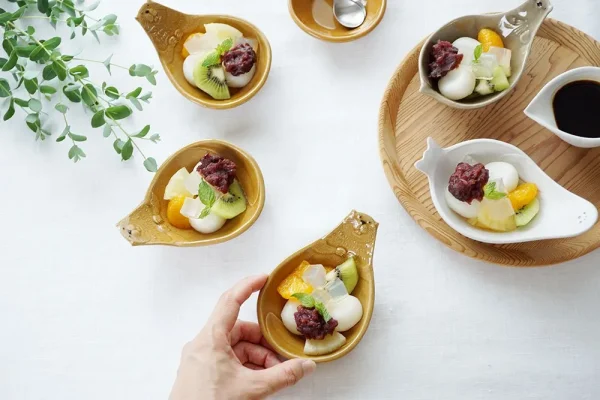 從上方視角顯示餐桌，前面的盤子被兩個手指握住，所有盤子上都有甜點 - Top view of a dining table, with the front plate held by two fingers and all plates featuring desserts.