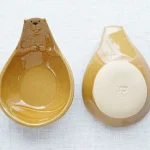 兩個Yoshizawa 益子燒海狸造型碗的正面和底部視圖，垂直展示 - Two Yoshizawa Mashiko-style beaver-shaped bowls shown vertically, one displaying the front and the other the bottom.