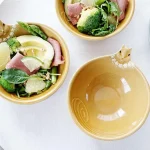 三個Yoshizawa 益子燒松鼠碗放在桌上，前面的碗是空的，設計清晰可見，後面的兩個碗裡裝有沙拉 - Three Yoshizawa Mashiko-style squirrel bowls on a table, with the front bowl empty and the design clearly visible, while the two back bowls contain salad.