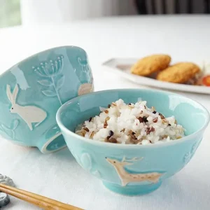 Yoshizawa 益子燒森林動物飯碗內裝米飯，並展示兩個不同側面的碗，擺放在餐桌上。 / Yoshizawa Mashiko-style forest animal rice bowl filled with rice, featuring two bowls shown from different sides on a dining table.