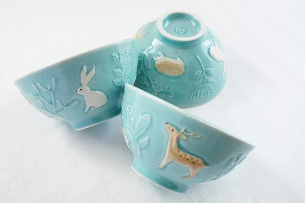 三個碗擺放在桌上,展示不同側面和碗邊的動物圖案,背景為白色。 / Three bowls arranged on a table showing different sides and animal patterns on the sides, with a white background