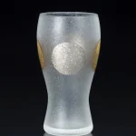日本製 ADERIA 石塚硝子 金箔日月紋磨砂啤酒杯有銀色圓形圖案的的一面，背景為黑色。