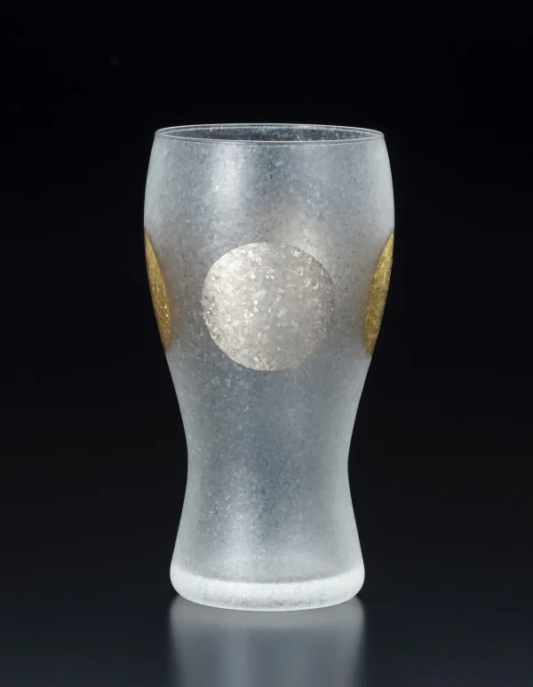 日本製 ADERIA 石塚硝子 金箔日月紋磨砂啤酒杯有銀色圓形圖案的的一面，背景為黑色。