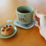 手上拿着綠色CDF ètendue I LOVE CAT！ 貓咪面圖案可堆疊陶瓷杯,杯裏面裝着茶.